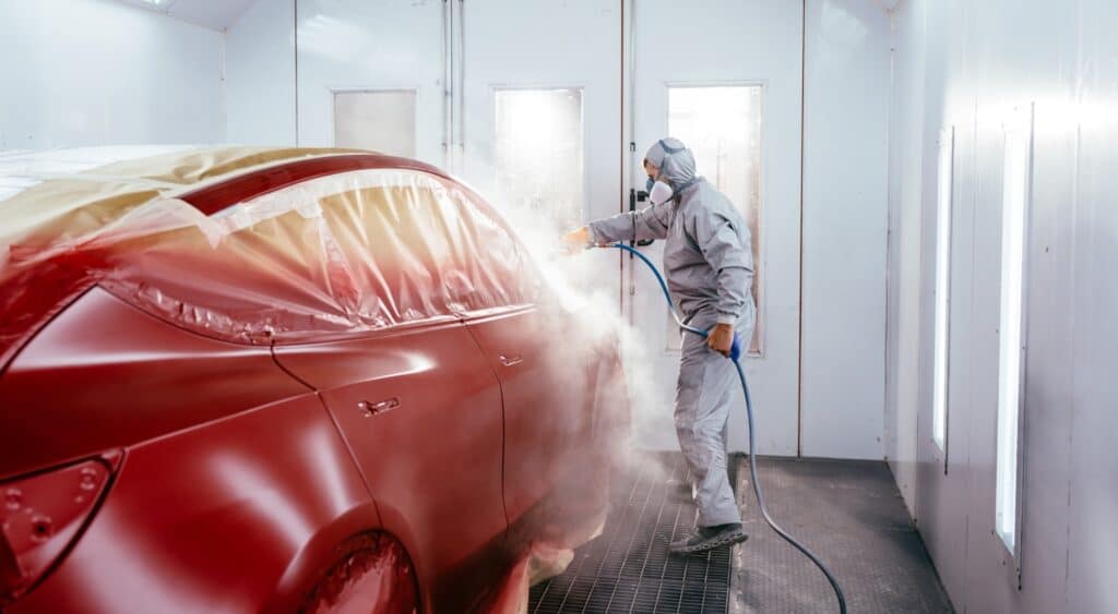 Person lackiert ein Auto rot in einer Lackierkabine
